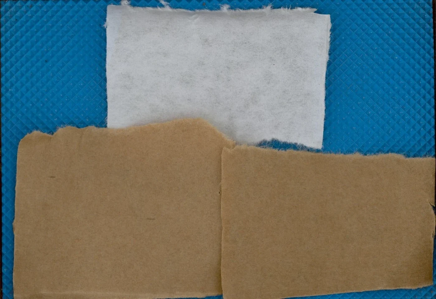 Composição em cores de uma folha de papel branco, acima, e de duas metades de papel marrom, abaixo, sobre o fundo azul do equipamento